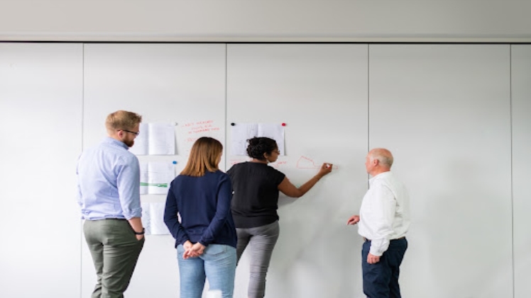 Four people discussing strategic account planning tips at a white wall.